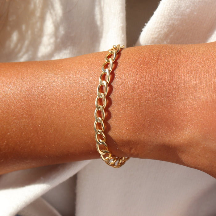 Model wearing a 14k gold fill chunky curb chain bracelet with polished flat links, styled on the wrist in warm natural sunlight.