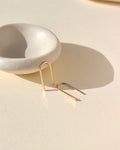 arch shaped 14k solid gold earrings near a small dish in the sunlight