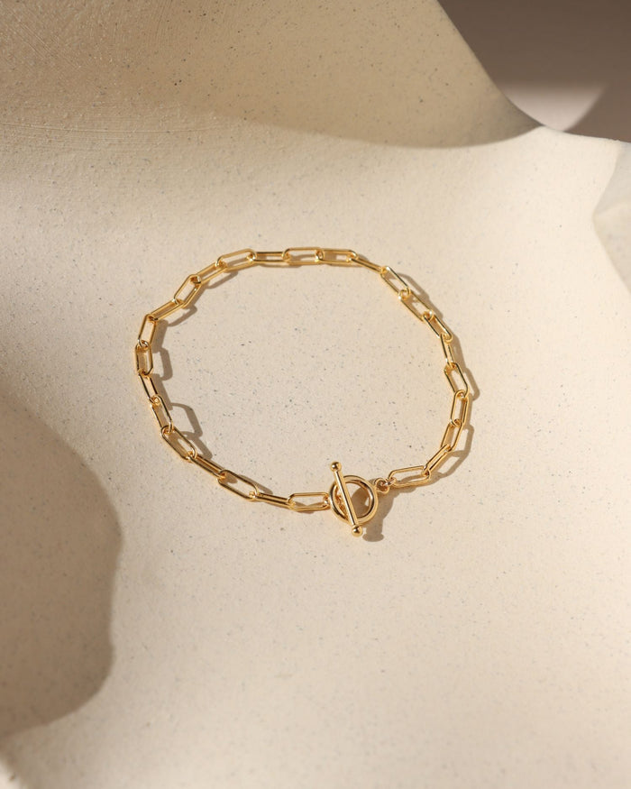 gold paperclip chain bracelet with toggle clasp in the sunlight on a light surface