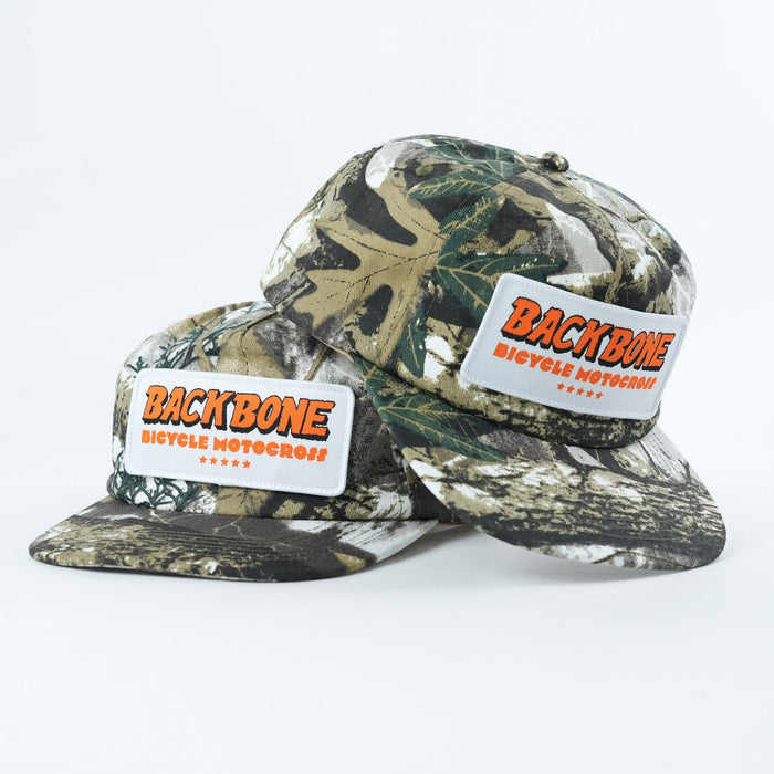 Two camouflage Backbone 5 Star Snapback Hats are stacked, each with a rectangular patch on the front reading "BACKBONE BICYCLE MOTOCROSS" in orange and white, representing classic Backbone BMX style.