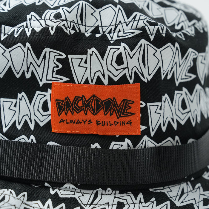 Close-up of a Backbone AO Boonie, showcasing a white "BACKBONE" graphic pattern and an orange patch with the words "BACKBONE ALWAYS BUILDING.