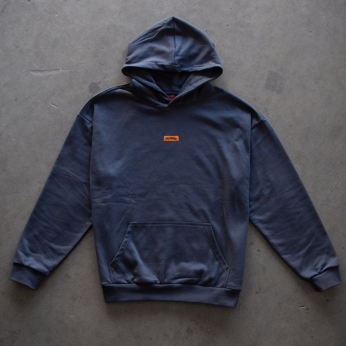 A Backbone In the Dirt Hoodie in dark gray, featuring a heavy weight design with a front pouch pocket and a small orange “Supreme” logo on the chest, displayed on a plain concrete surface.