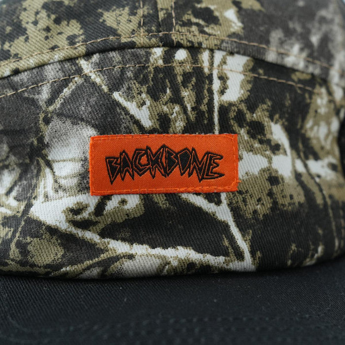 A close-up of the Backbone Ride Club Hat, a camouflage-patterned 5 panel cap featuring an orange patch with "BACKBONE" in bold, stylized lettering.