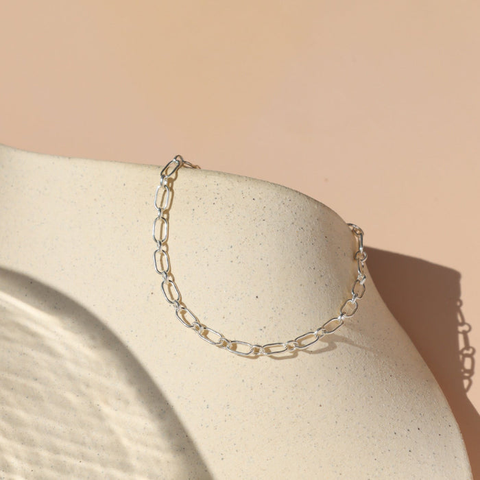 Timeless sterling silver oval linked chain bracelet on a beige dish with a tan background