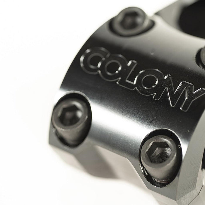 Close-up of a black metal BMX stem with four hex bolts and the word “COLONY” engraved on its surface. This is the Colony Variant 35mm Stem (22.2mm Clamp), recognized for its precise engineering and 35mm reach.