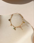 Gold chain linked bracelet with gemstone charms evenly spaced across it, laid on a beige dish in the sunlight