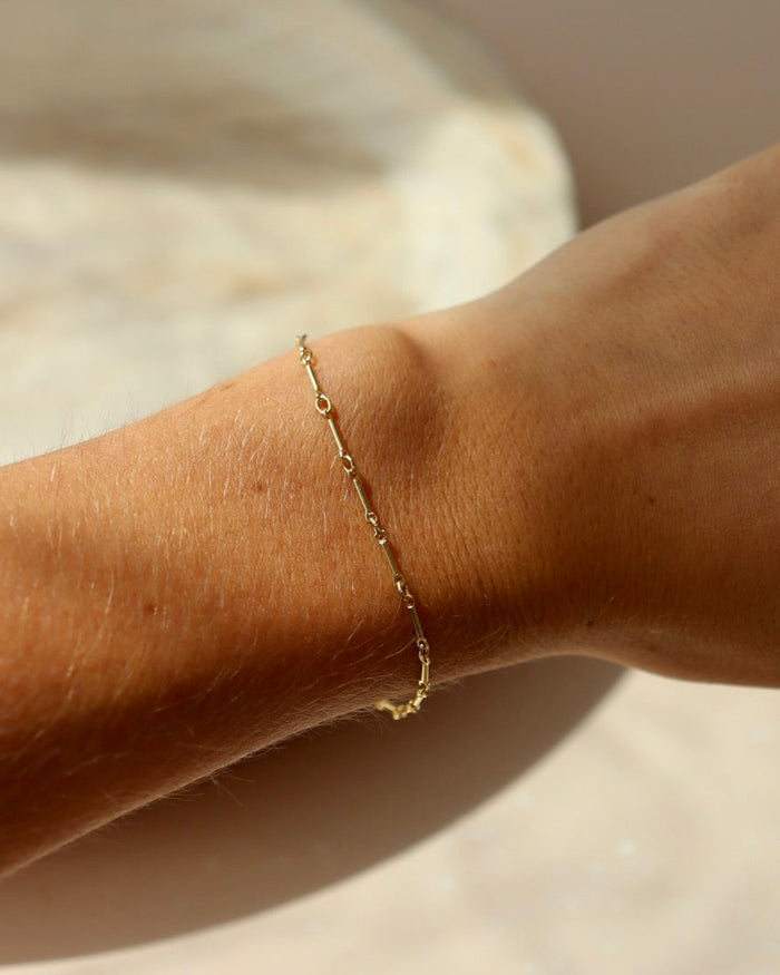 Model wearing 14k gold fill dot + dash bracelet. This is a gold bar link chain. Model is wearing a light purple tank top.