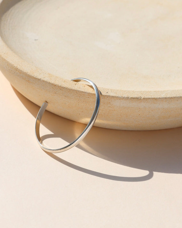 925 sterling silver stacking cuff placed on beige dish, set in the sunlight.