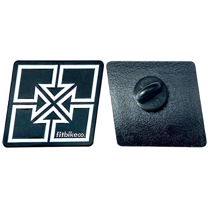 The Fit Bike Co Key Enamel Pin is shown: one side displays a white geometric cross with "fitbikeco." text, while the other side shows the black metal back and clasp.