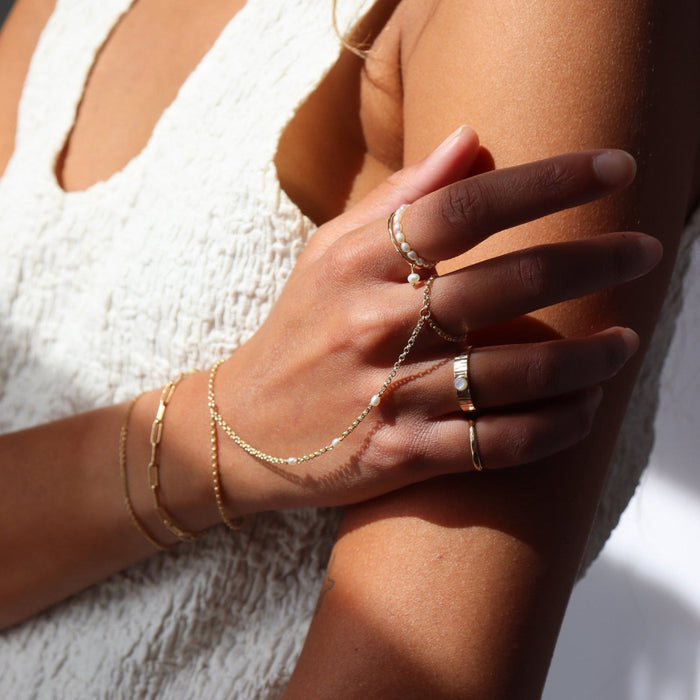 Model wearing 14k gold fill hand chain with pearls paired with other 14k gold fill jewelry