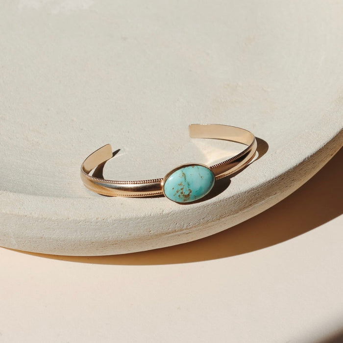 14k Gold Fill bezel set turquoise cuff on a thick smooth band with textured edges on a beige background in the sunlight