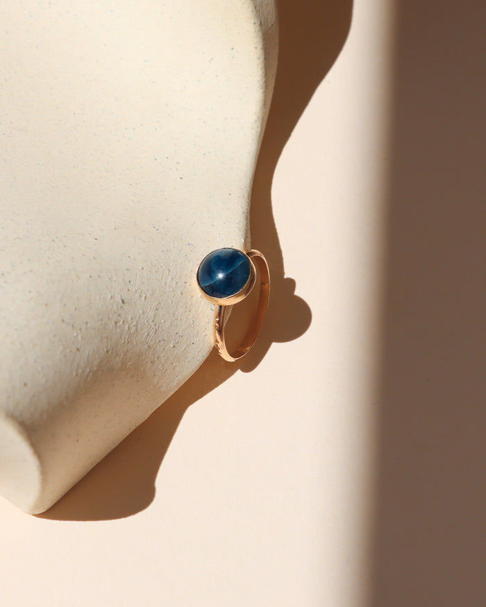 14k gold fill ring with round blue stone on a light dish