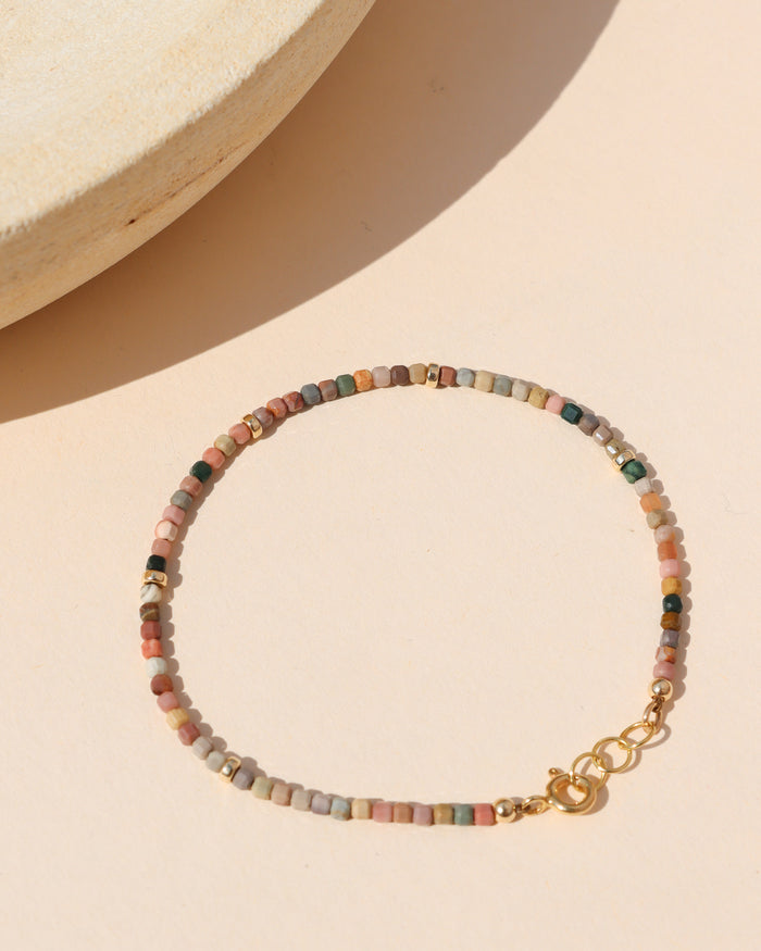 tiny agate beaded bracelet with gold accents on a light surface in the sunlight