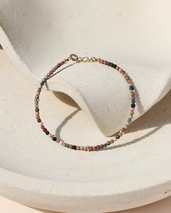 tiny agate beaded bracelet with gold accents on a light wavy dish in the sunlight