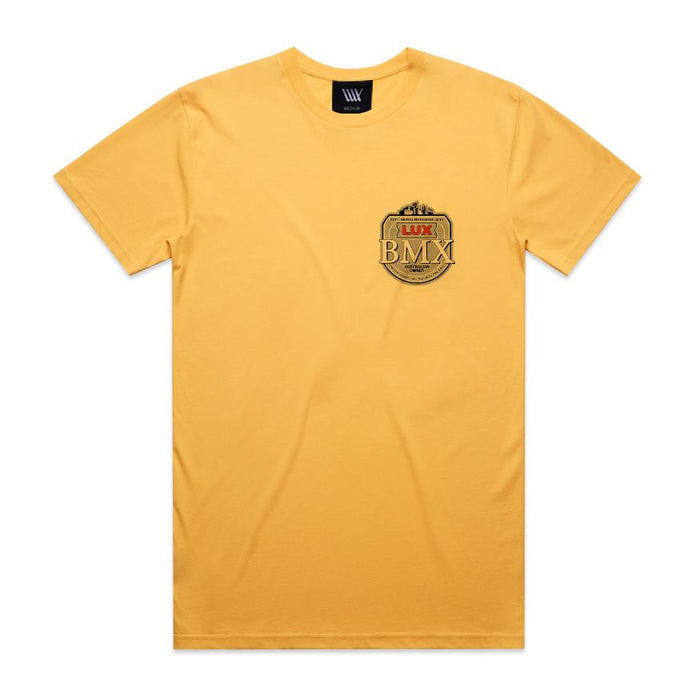 The LUXBMX Gold Tee Sunset is a yellow classic crew tee featuring a small black and gold "LUX BMX" badge on the left chest—a true Brisbane icon. It also includes a black neck label and no other visible designs.