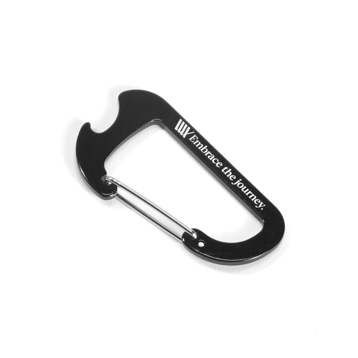 A black metal carabiner with a bottle opener and "Embrace the journey." printed on the side—an essential in the LUXBMX Journey Explorer Bundle.
