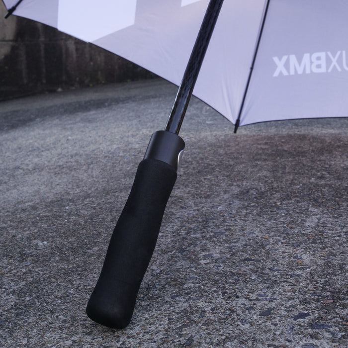 Close-up of a LUXBMX Race Track Umbrella handle on a textured outdoor surface, with the premium carbon pole umbrella open in the background.