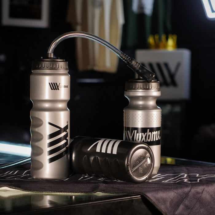 Three silver 500ml LUXBMX Squirt Water Bottles made from BPA free plastic are displayed on a dark surface; one has a flexible straw and another lies horizontally.