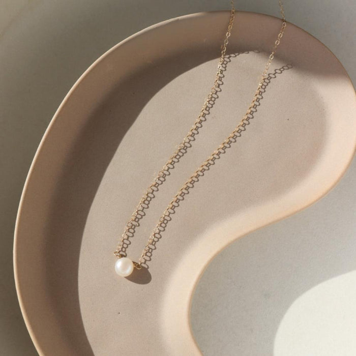 mother of pearl bead wrapped onto a dainty 14k solid gold necklace chain laid on a light dish