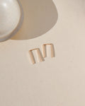 14k gold fill mini staple shaped earrings laid by small dish in the sunlight