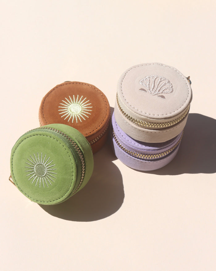 A collection of mini travel jewelry cases with embroidered sun designs, stacked together. They come in beige, green, brown, and purple colors.