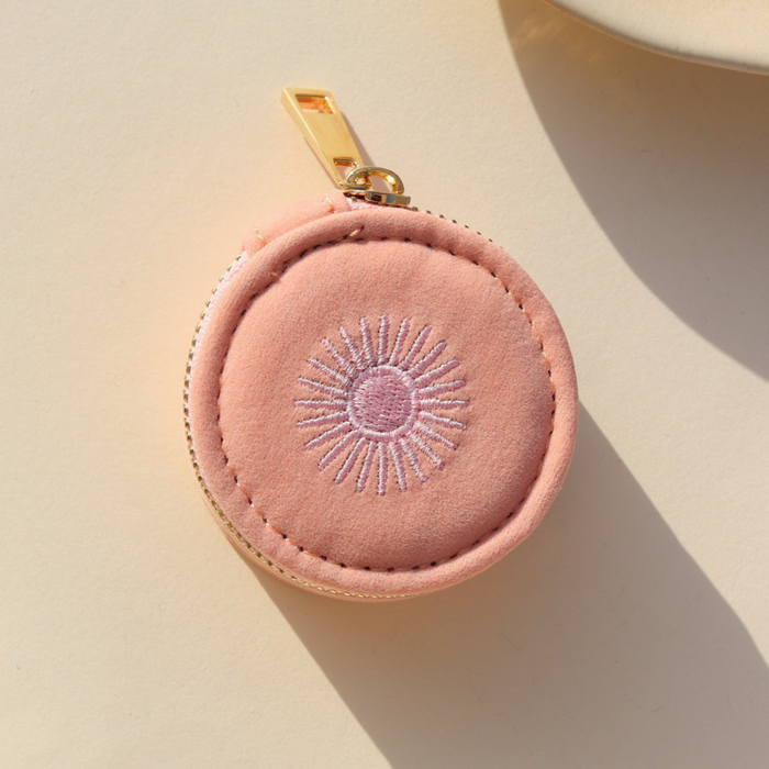Pink round jewelry case with gold zipper on a beige background