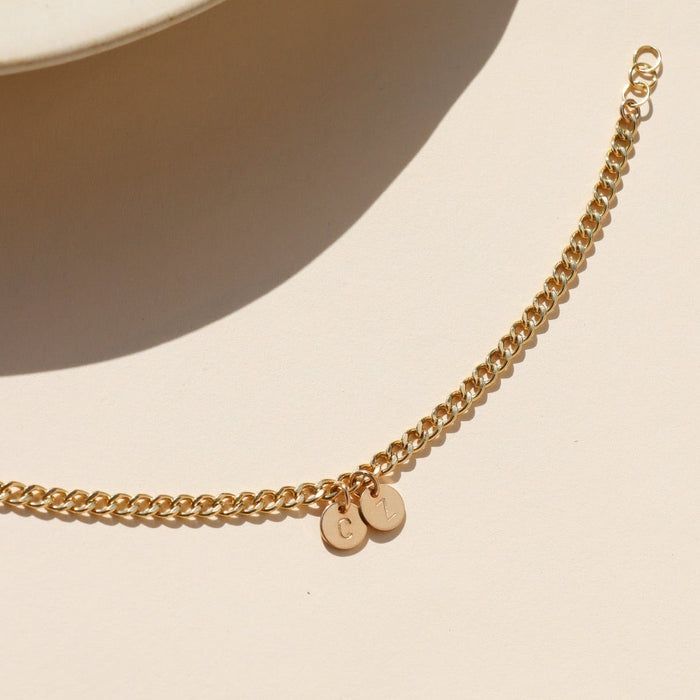 14k gold fill curb chain bracelet with hand stamped round disc charms on a light table