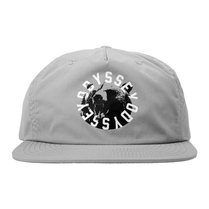 The Odyssey Bear Central 5 Panel Hat is a light gray cap featuring a circular bear face logo with “ODYSSEY” repeated around it in white, adding fresh style to your look.