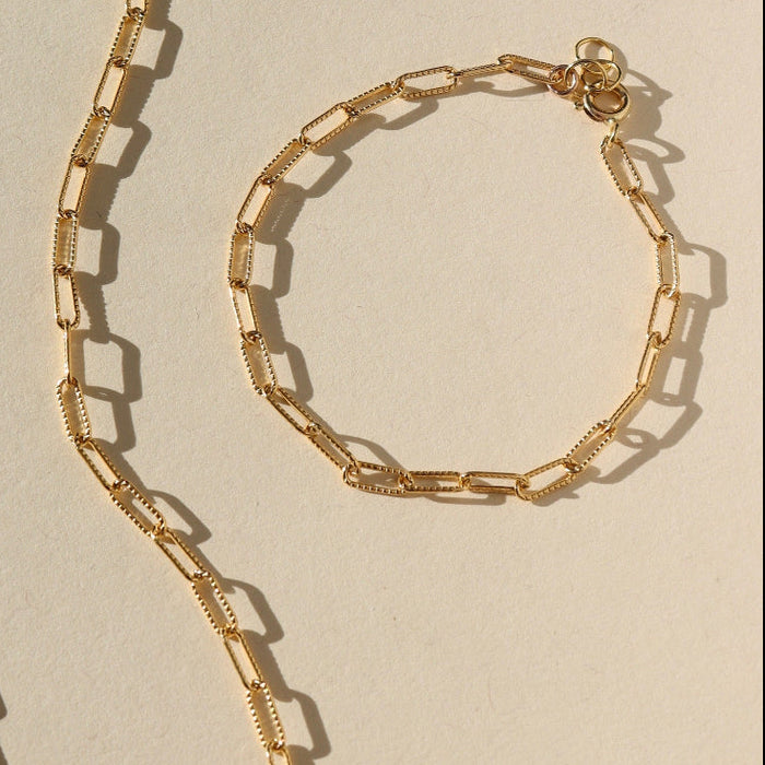 Gold chain necklace and bracelet on a beige background