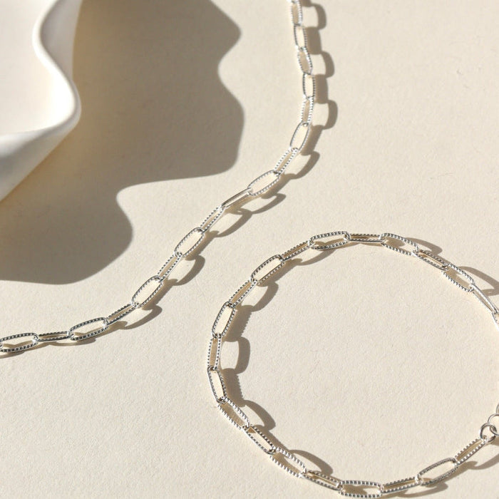 Silver chain necklace and bracelet on a beige background