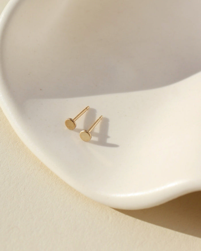 14k gold fill polka dot studs laid on white wavy dish in sunlight