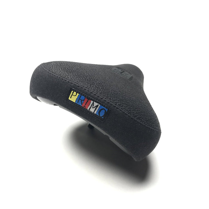 The Primo HD Pivotal Seat is a black bike seat with a textured surface and a small rectangular “PRIMO” logo in yellow, blue, and red on the back. Durable and designed for pivotal seat compatibility, it is shown against a white background.