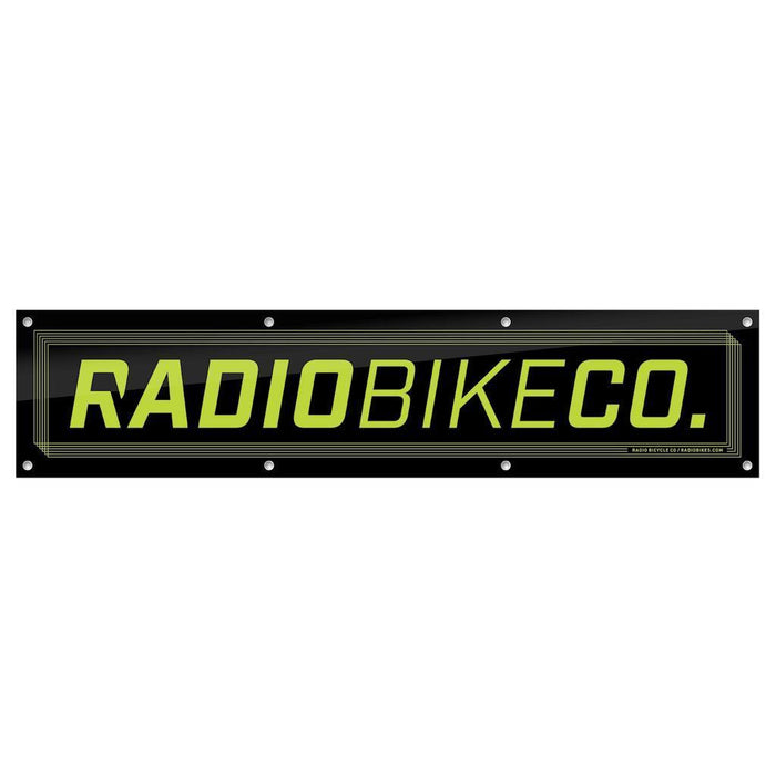 The Radio Contest Banner is a rectangular black PVC sign with yellow-green "RADIOBIKECO." text and edge mounting holes—ideal for outdoor use or displaying your favorite BMX brand.