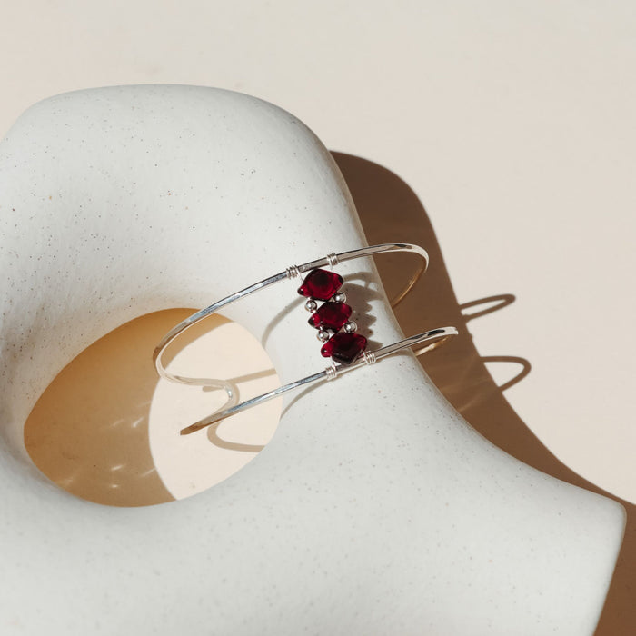 sterling silver cuff bracelet with three ruby gemstones on a light dish