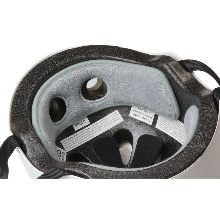 A close-up of the interior of a white bicycle helmet, showing grey padding, ventilation holes, and adjustable black straps. Labels with product and safety information are visible, alongside an S-One Helmet Wide Terry Cloth Liner that ensures comfort on every ride.