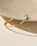 14k gold filled cuff with lightly hammered texture leaned on a beige ceramic dish in the sunligjt.