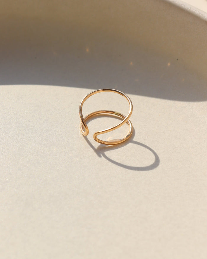 14k gold fill hammered and hand shaped ring laid on a tan plate in the sunlight