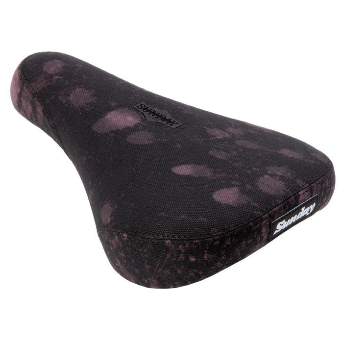 The Sunday Pivotal Seat (Brett Silva Signature) is a black bike seat with a faded pink pattern and "Sunday" branding on the top and side, designed specifically for Sunday Pivotal setups.