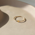 14k gold fill Tiny heart ring laid on a tan plate in the sunlight. This ring features a smooth band with a tiny heart. This ring is so cute stacked with any of the stacking rings at Token Jewelry.