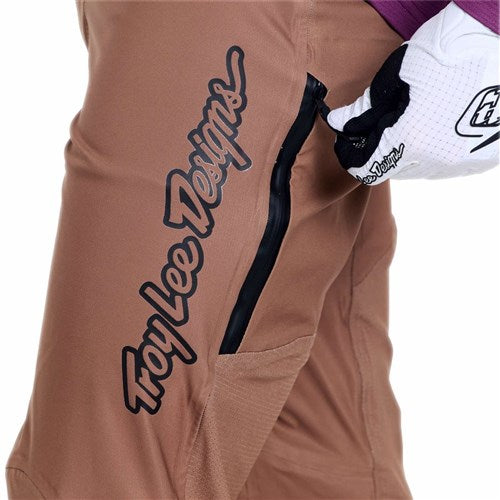 Wearing TLD 26.1 Sprint Pro Pants / Mono Sienna made with 4-way stretch fabric, a person in a white glove unzips the black pocket zipper.