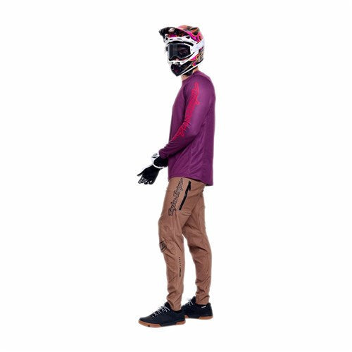 A person wearing a pink helmet, goggles, magenta long-sleeve shirt, black gloves, and TLD 26.1 Sprint Pro Pants / Mono Sienna made from 4-way stretch fabric stands sideways against a white background.