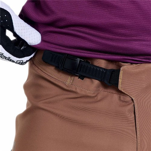 Close-up of a person wearing TLD 26.1 Sprint Pro Pants / Mono Sienna, crafted from durable 4-way stretch fabric, styled with a black adjustable belt and purple shirt. A white and black glove is tucked at the waist.