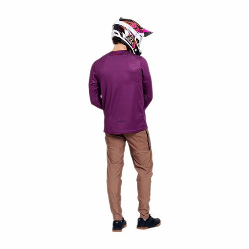 A person in a purple long-sleeve shirt, black shoes, and a motocross helmet stands with their back to the camera against a white background, showcasing TLD 26.1 Sprint Pro Pants / Mono Sienna made from durable 4-way stretch fabric.